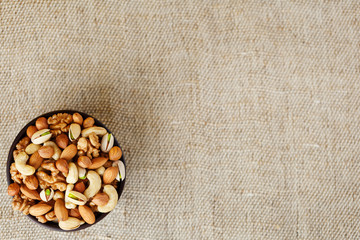 Mix of various nuts in a wooden cup against the background of fabric from burlap. Nuts as structure and background, macro. Top view.