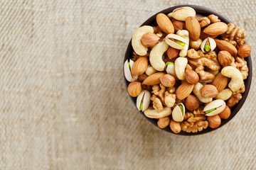 Mix of various nuts in a wooden cup against the background of fabric from burlap. Nuts as structure and background, macro. Top view.