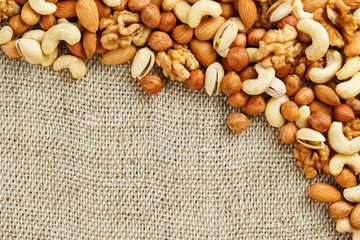 Mix of nuts of cashew, almonds, pistachios, hazelnuts and walnuts is against the background of brown fabric of burlap. Nuts as structure and background, macro