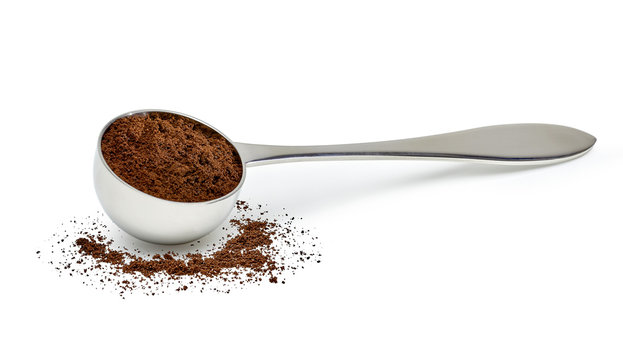 Grinded coffee powder in measuring scoop with beans isolated on white background