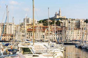 Pleasure boats moored in the marina of the Old Port of Marseille, France, with Notre-Dame de la Garde basilica on top of the hill at sunset.