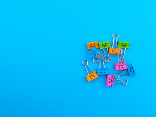 Funny smile yellow red green metal binder clip or multicolored paperclip on blue background with copyspace for text