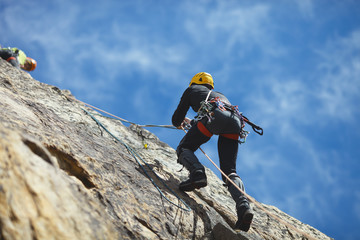 Climber climbs on the rock wall against a blue sky. Climbing gear. Climbing equipment.
