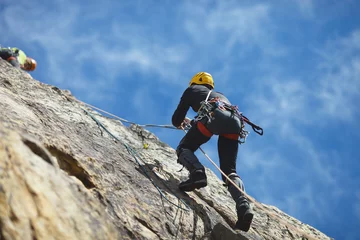 Foto auf Acrylglas Kletterer klettert auf die Felswand vor blauem Himmel. Kletterausrüstung. Kletterausrüstung. © esalienko