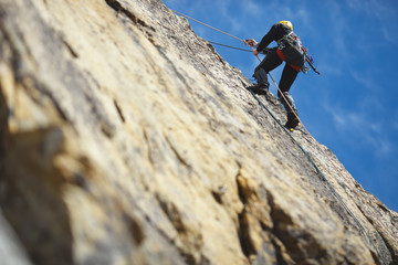 Climber climbs on the rock wall against a blue sky. Climbing gear. Climbing equipment.