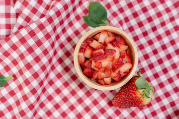 The dice or chopped strawberry put in wooden bowl and placed on a plaid tablecloth.