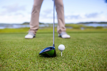 golf club and golf ball on tee, focus on the head of the club and ball.