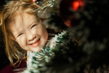 Little girl sit under the Christmas tree in the morning rays of the Christmas sun. Christmas tale.