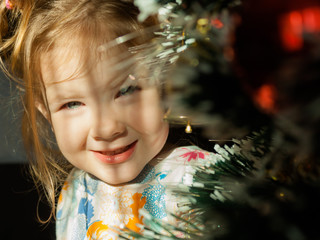 Little girl sit under the Christmas tree in the morning rays of the Christmas sun. Christmas tale.