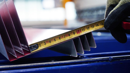 hand using a metal tape measure on sheet metal in close up selective focus shot. industrial background concept.