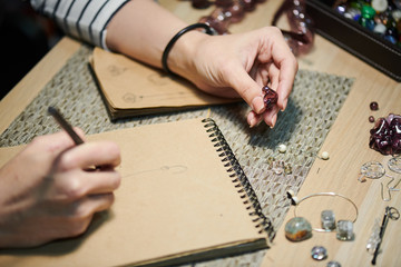 Closeup of unrecognizable woman drawing sketches while creating beautiful handmade jewelry, copy...