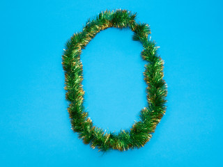 number zero 0 made of green Christmas tree tinsel on blue background
