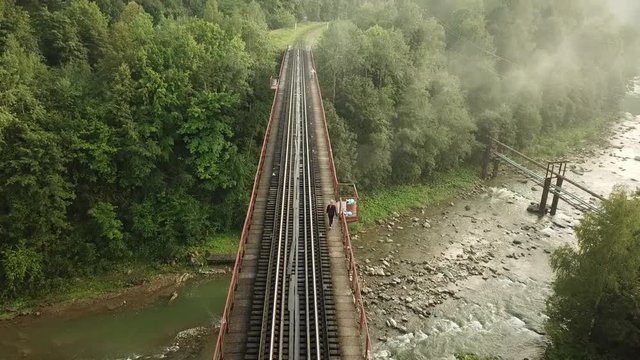 Aerial footage of a woman walking on the tracks of a railway bridge over the Prut River in Yaremche, the city on the Carpathian Mountains in Ukraine.