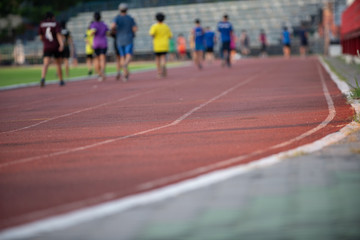 Groups of jogging people, with a variety of ages and sizes, running on the track in a stadium during the evening time with sun set.