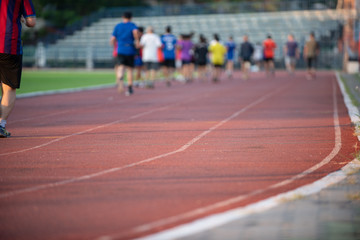 Groups of jogging people, with a variety of ages and sizes, running on the track in a stadium during the evening time with sun set.