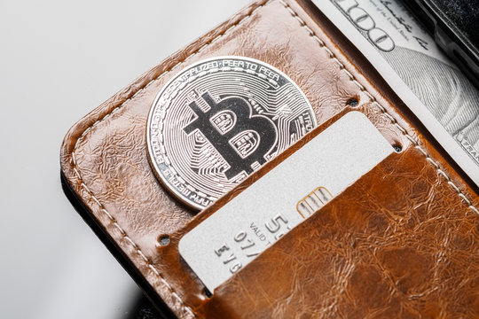 Popular cryptocurrency in leather wallet. Silver coin with bitcoin symbol cash and credit / debit cards.