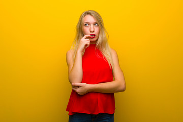 Young girl with red dress over yellow wall having doubts while looking up