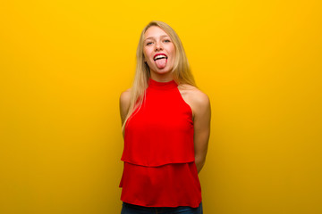 Young girl with red dress over yellow wall showing tongue at the camera having funny look