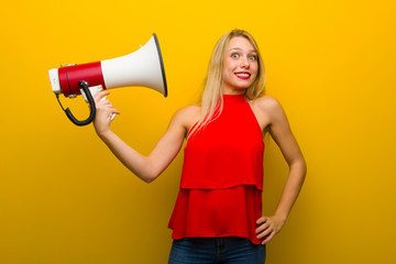 Young girl with red dress over yellow wall taking a megaphone that makes a lot of noise