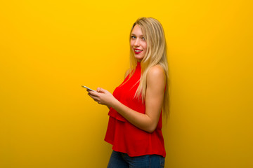 Naklejka premium Young girl with red dress over yellow wall sending a message with the mobile