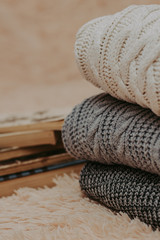 Folded knitted woolen sweaters, stack of old books on a cozy fluffy beige blanket
