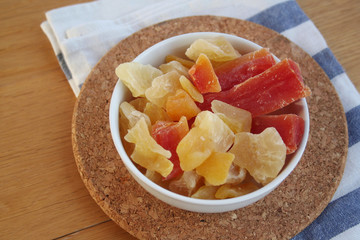 Candied and dried papaya, pineapple and mango pieces in a bowl on wooden table
