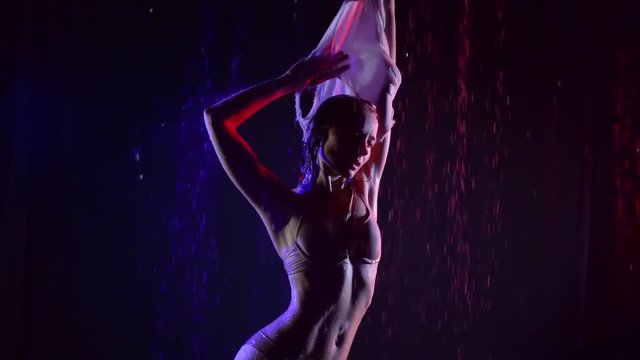 Sexy female model taking shirt off while posing under rain in studio, art fashion shot.