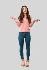 Full body of Teenager girl with pink shirt having doubts while raising hands and shoulders on isolated grey background