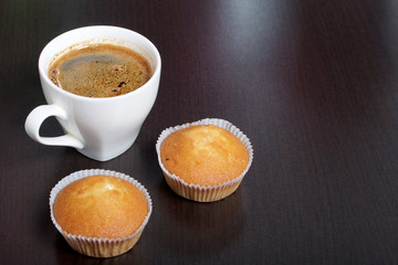 A cup of freshly brewed coffee and muffins. On a dark background.