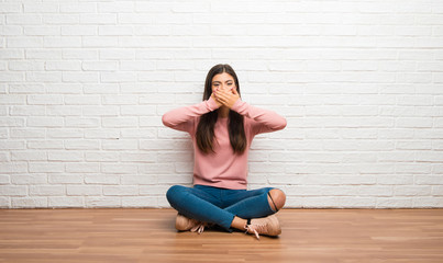 Teenager girl sitting on the floor in a room covering mouth with hands for saying something inappropriate