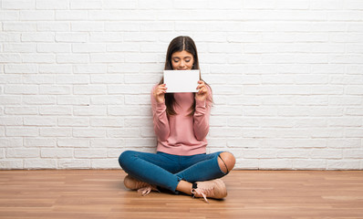Teenager girl sitting on the floor in a room holding a placard for insert a concept