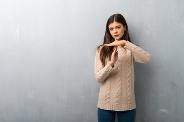 Teenager girl with sweater on a vintage wall making stop gesture with her hand to stop an act