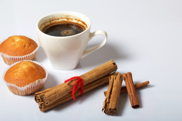 A cup of freshly brewed coffee and muffins. Nearby are cinnamon sticks. On a white background.
