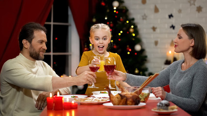 Parents clinking wine on Xmas eve, kid drinking juice, happy family celebrating