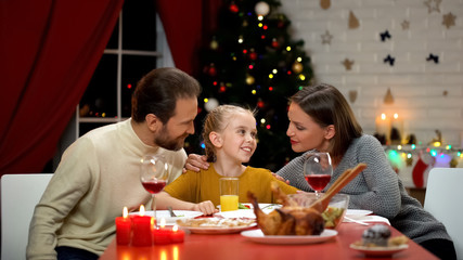 Parents hugging daughter at Xmas lunch, happy family celebrating holiday eve
