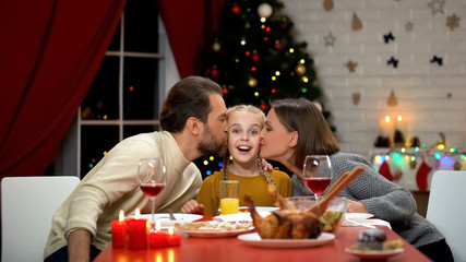 Parents kissing smiling daughter at Christmas dinner, family relationships
