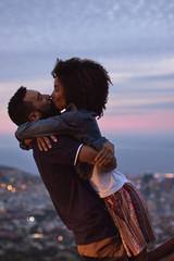Woman with afro kisses boyfriend in fading light city in background