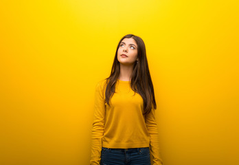 Teenager girl on vibrant yellow background looking up with serious face