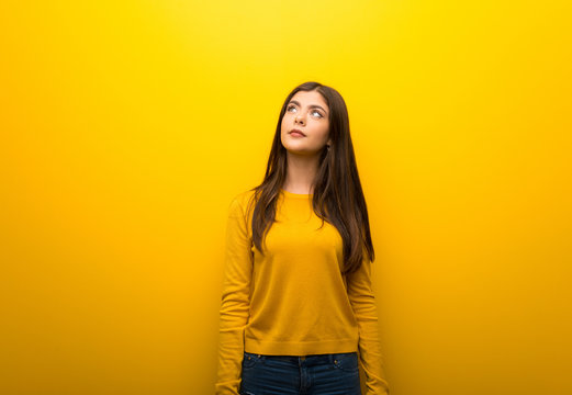 Teenager Girl On Vibrant Yellow Background Looking Up With Serious Face