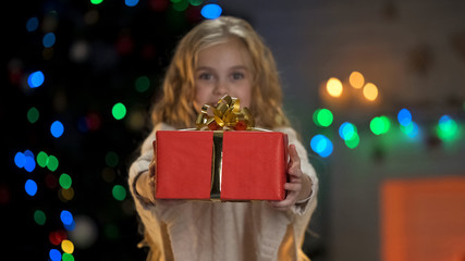 Fototapeta na wymiar Cute blond girl showing Christmas gift to camera, miraculous holiday atmosphere