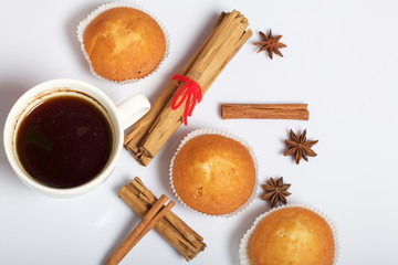 A cup of freshly brewed coffee and muffins. Nearby are cinnamon sticks and anise stars. On a white background.