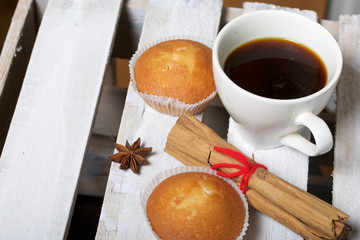 A cup of freshly brewed coffee and muffins. Nearby are cinnamon sticks and anise stars. Located on a wooden box.