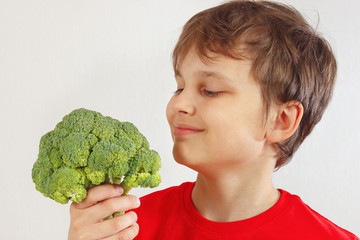 Little funny boy in a red shirt with broccoli on a white background