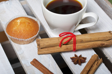 A cup of freshly brewed coffee and muffins. Nearby are cinnamon sticks and anise stars. Located on a wooden box.