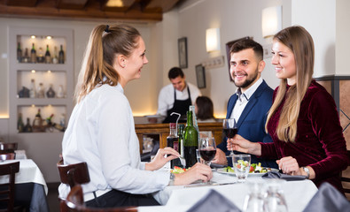 Group of happy friends enjoying evening meal at restaurant