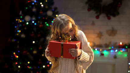 Obraz na płótnie Canvas Cute little girl hugging Christmas present, dream come true, festive atmosphere