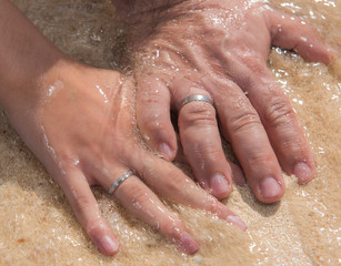 Fototapeta premium Bride and grooms hands together on sandy beach showing rings