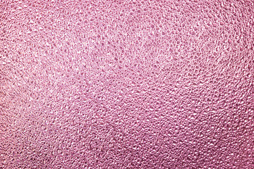 Structural glass surface in pink or purple color. Fine texture on the glass have geometric shapes. Empty color background.