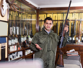 Young male hunter choosing shotgun in store