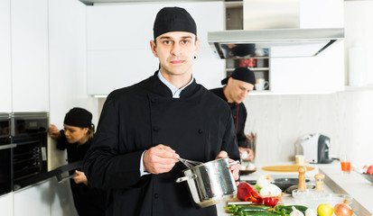 Portrait of man cook who is standing with pot for soup on his work place in the kitchen